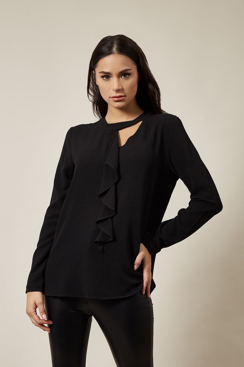 Pode incluir: Uma blusa preta de manga comprida com gola de babados e um decote de olho de fechadura. A blusa tem um caimento solto e &eacute; feita de um tecido macio e confort&aacute;vel.