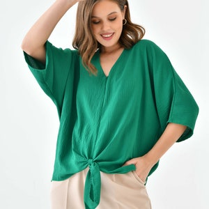 May include: A green, loose-fitting, short-sleeved blouse with a knotted front. The blouse is made of a textured fabric and has a v-neck.