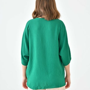 May include: A green, long-sleeved blouse with a v-neckline. The blouse is made of a textured fabric and has a relaxed fit.