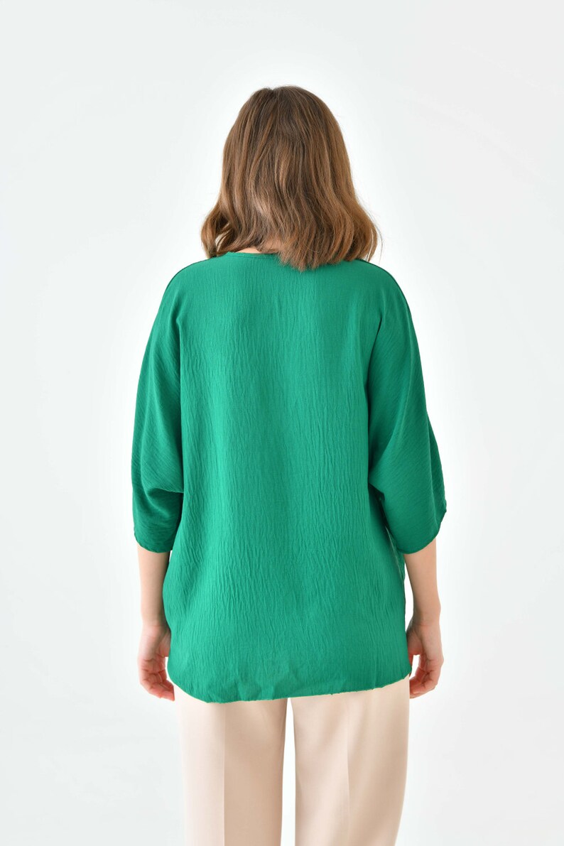 May include: A green, long-sleeved blouse with a v-neckline. The blouse is made of a textured fabric and has a relaxed fit.