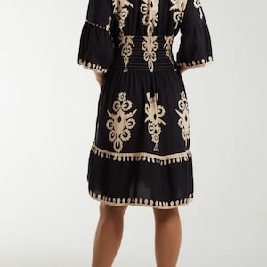 Puede incluir: Un vestido negro y beige con estampado, cintura fruncida y falda de vuelo. El vestido tiene cuello en V y mangas 3/4.