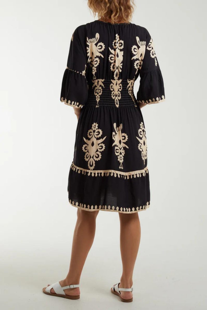 Puede incluir: Un vestido negro y beige con estampado, cintura fruncida y falda de vuelo. El vestido tiene cuello en V y mangas 3/4.