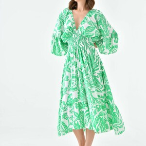 Puede incluir: Un vestido midi de estampado floral verde y blanco con cuello en V y mangas largas. El vestido tiene una cintura ajustada y una falda fluida.