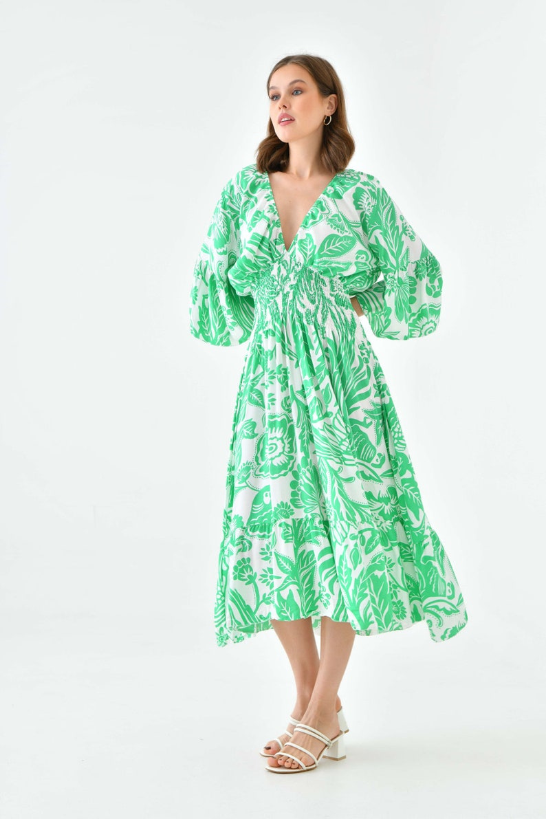 Puede incluir: Un vestido midi de estampado floral verde y blanco con cuello en V y mangas largas. El vestido tiene una cintura ajustada y una falda fluida.