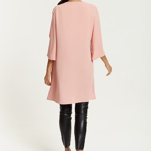 Op de afbeelding: Een lange, roze, vloeiende tuniek met een ronde hals en 3/4 mouwen. Het model draagt een zwarte legging en zwarte sandalen met hak.