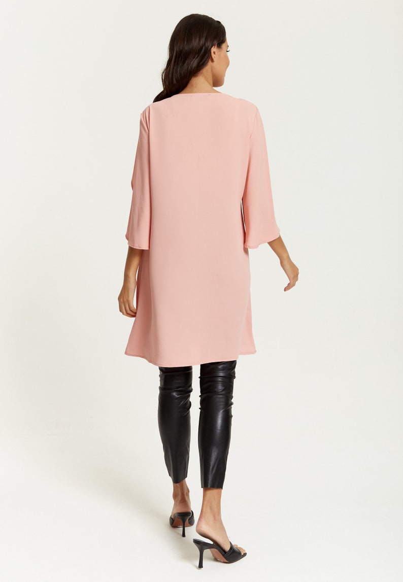 Op de afbeelding: Een lange, roze, vloeiende tuniek met een ronde hals en 3/4 mouwen. Het model draagt een zwarte legging en zwarte sandalen met hak.