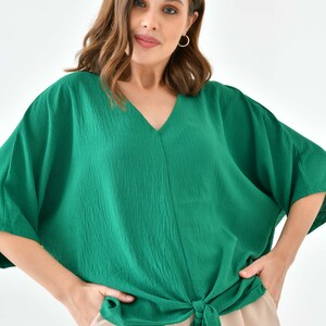 May include: A green, loose-fitting, short-sleeved blouse with a V-neck and a knotted front.