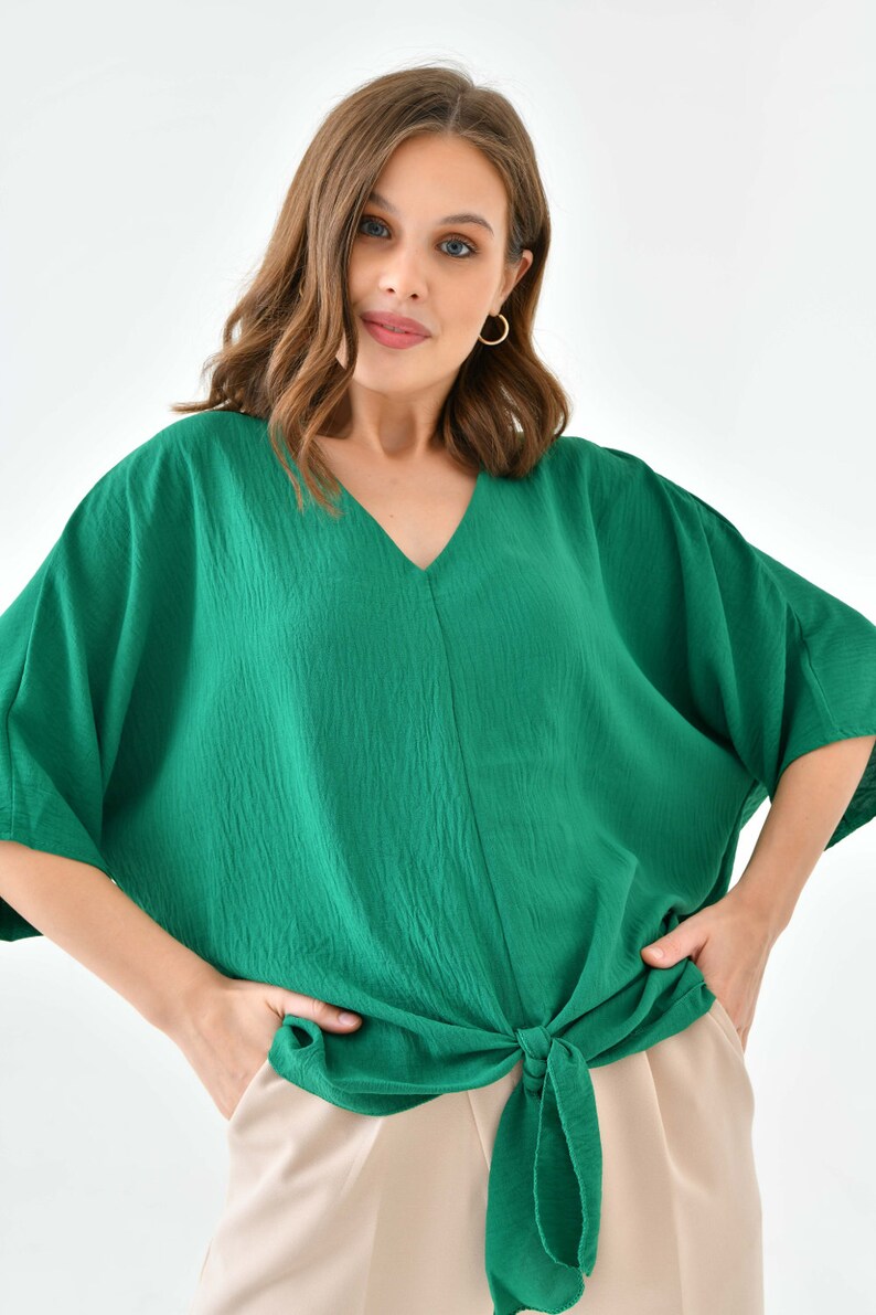 May include: A green, loose-fitting, short-sleeved blouse with a V-neck and a knotted front.