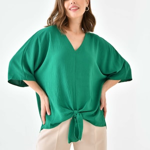 May include: A green, loose-fitting, v-neck top with a knotted front. The top has short, wide sleeves and is made of a textured fabric.