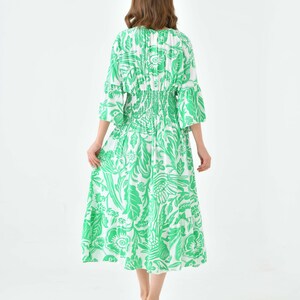 Puede incluir: Un vestido midi blanco con estampado floral verde. El vestido tiene una cintura fruncida y mangas 3/4.