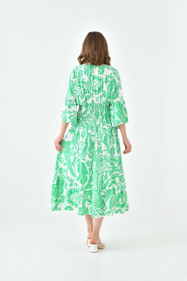 Puede incluir: Un vestido midi blanco con estampado floral verde. El vestido tiene una cintura fruncida y mangas 3/4.