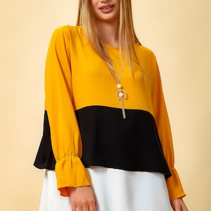 May include: A yellow, black and white layered tunic top with long sleeves and a gold chain necklace.