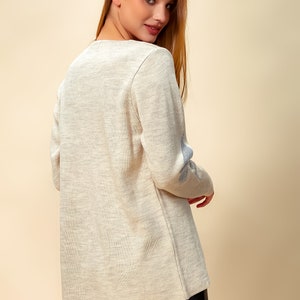 May include: A light beige long-sleeved sweater with a subtle texture and a blue embroidered design on the elbow.