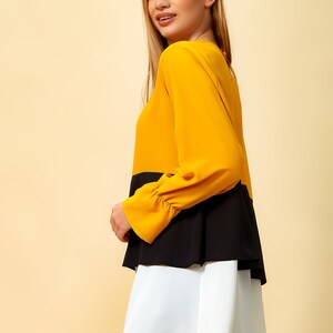 May include: A layered blouse with a mustard yellow top, black middle layer, and white bottom layer. The blouse has long sleeves with ruched cuffs.