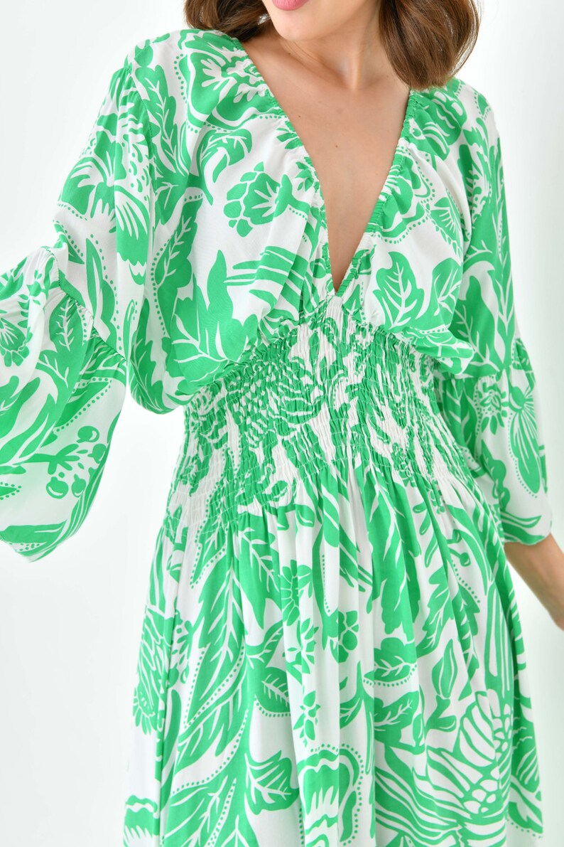 Puede incluir: Un vestido de estampado floral blanco y verde con escote en V y cintura fruncida.