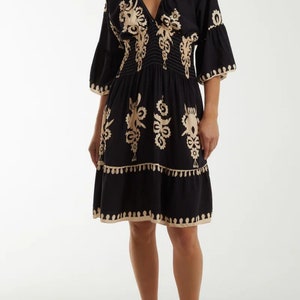Puede incluir: Un vestido negro corto con cuello en V y mangas 3/4. El vestido presenta un estampado floral bordado en beige y una falda de capas. El vestido est&aacute; ajustado a la cintura con una banda el&aacute;stica.