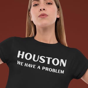 Op de afbeelding: Zwart T-shirt met de witte tekst "HOUSTON WE HAVE A PROBLEM". Het T-shirt heeft een ronde hals en wordt gedragen.