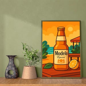 May include: A framed art print depicting a Modelo Especial beer bottle on a wooden surface, set against a beach scene. The artwork includes a slice of orange and a green leaf, with a warm colour palette.