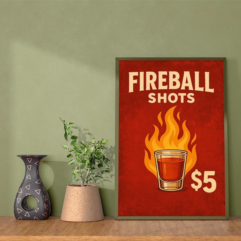 Może przedstawiać: Oprawiony plakat z napisem "FIREBALL SHOTS" białymi literami na czerwonym tle. Szklanka z płomieniami i cena "$5" są r&oacute;wnież wyświetlane. Po lewej stronie znajduje się dekoracyjny wazon i roślina doniczkowa.