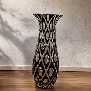 Könnte beinhalten: Eine hohe, ausgestellte Kristallvase mit einem tiefschwarzen Überfang, der durch Schliff das klare Glas freigibt. Die Oberfläche ist mit einem sich wiederholenden Rautenmuster verziert, wobei jede Raute ein vertikales ovales Schliffmotiv enthält.