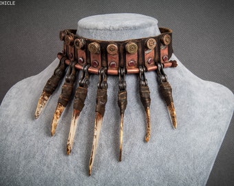 Op de afbeelding: Een bruine leren choker ketting met een ketting en metalen accenten. De ketting is versierd met patroonhulzen en bot-achtige spikes.