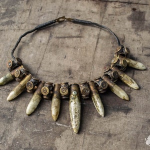 Op de afbeelding: Een ketting gemaakt van lege patroonhulzen en bot-achtige hangers. De ketting ligt op een houten oppervlak.