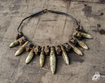 Op de afbeelding: Een ketting gemaakt van lege patroonhulzen en bot-achtige hangers. De ketting ligt op een houten oppervlak.