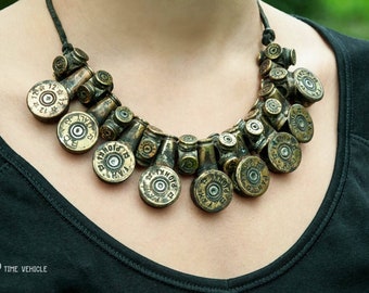 Op de afbeelding: Een ketting gemaakt van geweerschotenhulzen. De hulzen zijn in een cirkelvormige opstelling gerangschikt en met een bruin koord verbonden. De ketting wordt gedragen door een persoon met een zwart shirt.