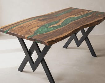 May include: A rectangular dining table featuring a natural live-edge wood slab with a prominent central inlay of translucent green resin. The table is supported by two black metal legs designed in a geometric, angular zigzag pattern.