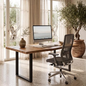 May include: A rectangular wooden desk with a natural live edge and black metal U-shaped legs. On the desk sits a silver computer monitor, a keyboard, a mouse, and a small ceramic vase with a branch. A black mesh office chair with wheels is placed.