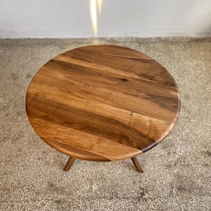 Top angle view of round solid walnut dining table showcasing natural wood grain variations, smooth handcrafted surface, and warm walnut tones, circular tabletop with organic flowing patterns and softly rounded edge detail, minimal and clean composition without additional elements, sculptural base subtly visible beneath, ideal for kitchen, dining room, or small space interiors, durable hardwood construction with timeless design and custom size options available
