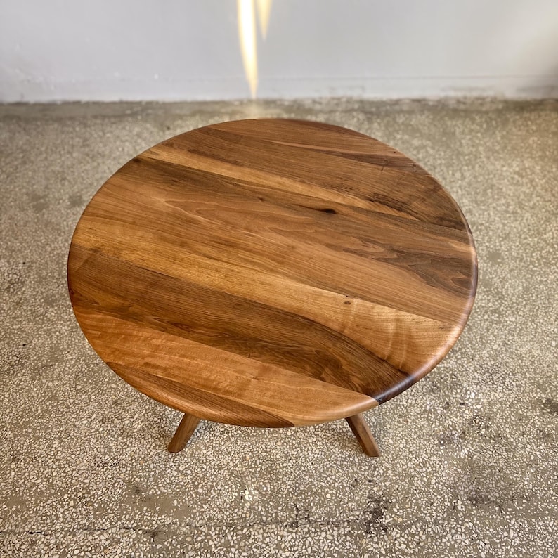 Top angle view of round solid walnut dining table showcasing natural wood grain variations, smooth handcrafted surface, and warm walnut tones, circular tabletop with organic flowing patterns and softly rounded edge detail, minimal and clean composition without additional elements, sculptural base subtly visible beneath, ideal for kitchen, dining room, or small space interiors, durable hardwood construction with timeless design and custom size options available