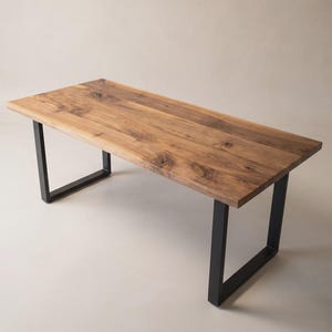 Op de afbeelding: Een rechthoekige eettafel met een blad van natuurlijk hout met een boomstamrand, zichtbare nerven en knoesten, ondersteund door twee zwarte, U-vormige metalen poten. Het tafeloppervlak heeft warme bruine tinten en een gladde afwerking.