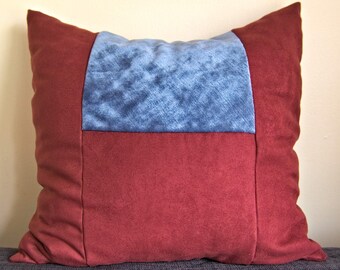 Könnte beinhalten: Ein Dekokissen in Burgunderrot und Blau mit geometrischem Muster. Das Kissen ist aus einem weichen, strukturierten Stoff.