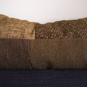 May include: A brown and beige patchwork cushion with a textured fabric. The cushion is made of different fabrics with different textures and patterns.