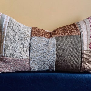 Peut inclure: Un coussin décoratif avec un motif patchwork composé de différents tissus de couleur marron, beige et gris. Le coussin a une forme rectangulaire et est fait d'un matériau doux et texturé.