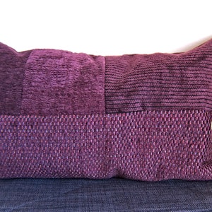 Puede incluir: Una almohada rectangular de color morado con tejido texturizado. La almohada está hecha de diferentes piezas de tela cosidas juntas.