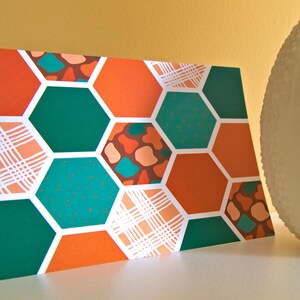May include: A card featuring a honeycomb pattern in shades of orange, green, and brown. The card has a white background and is made of paper.
