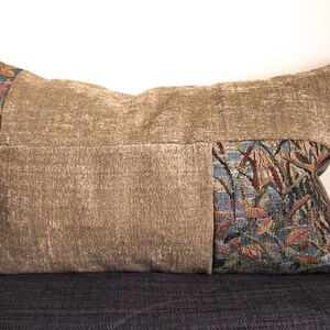 May include: A brown and beige throw pillow with a tapestry design on one side. The tapestry features a floral pattern in shades of blue, green, and brown.