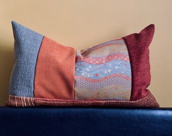 Könnte beinhalten: Ein Patchwork-Kissen in Blau-, Rot- und Brauntönen. Das Kissen hat ein geometrisches Muster und ist aus verschiedenen Stoffen gefertigt.
