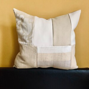 May include: A beige and white patchwork cushion with a floral pattern on one side. The cushion is made of different fabrics and textures.