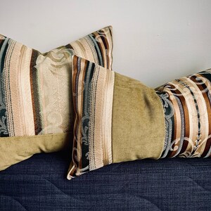 May include: Two decorative throw pillows with a striped pattern in shades of brown, beige, and green. The pillows have a subtle floral design and a velvet-like texture.