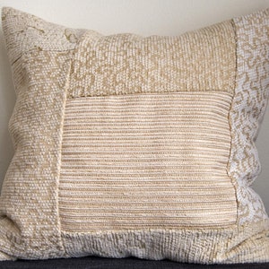 Peut inclure: Un coussin beige et blanc à motifs avec un tissu texturé. Le coussin est composé de différents morceaux de tissu cousus ensemble.