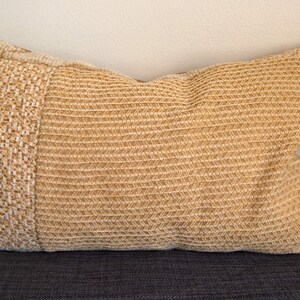 Peut inclure: Un coussin rectangulaire décoratif avec une texture tissée dans des tons beige et marron clair. Le coussin présente un panneau texturé contrastant à une extrémité, ajoutant un intérêt visuel. Le coussin est conçu pour la décoration intérieure.