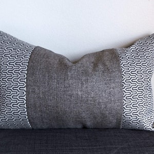 May include: A grey and white patterned throw pillow with a geometric design. The pillow is made of a soft, textured fabric.