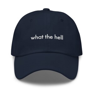 Puede incluir: Una gorra de b&eacute;isbol azul marino con texto bordado en blanco que dice "what the hell".