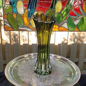 May include: A green glass vase with a fluted design and a scalloped rim. The vase is sitting on a silver tray with an ornate design.