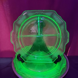 May include: A vibrant neon green glass divided serving plate featuring a scalloped edge and intricate embossed patterns. The plate is segmented into three sections by a central divider and displays a bright, glowing appearance under UV light.