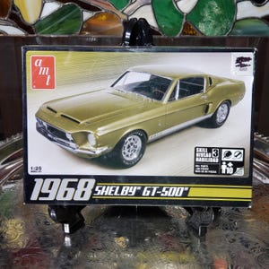 May include: A model kit box featuring a gold 1968 Shelby GT-500 car. The box displays the car's details, including the Shelby GT-500 logo and the scale of 1:25. The box also indicates a skill level of 3 and includes the AMT logo.