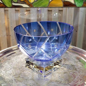 May include: A blue glass bowl with a white geometric pattern and a clear glass base. The bowl is sitting on a silver tray.